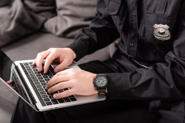 Police officer typing on a laptop on his lap